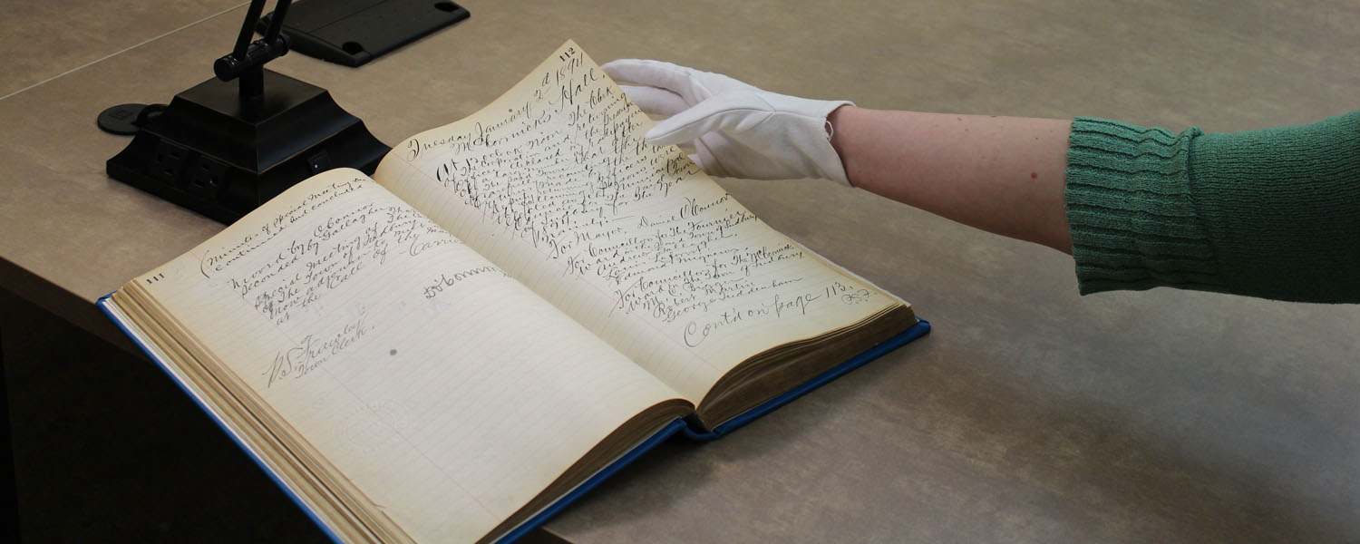 Gloved hands turning pages of a document at the Greater Sudbury Archives.